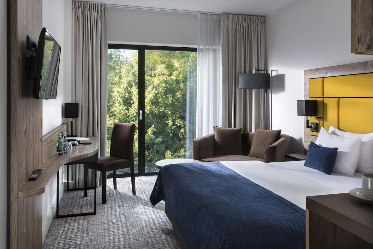 Ein Hotelzimmer mit einem großen Bett, einem Schreibtisch mit Stuhl, einem Fernseher und Blick auf Grün.