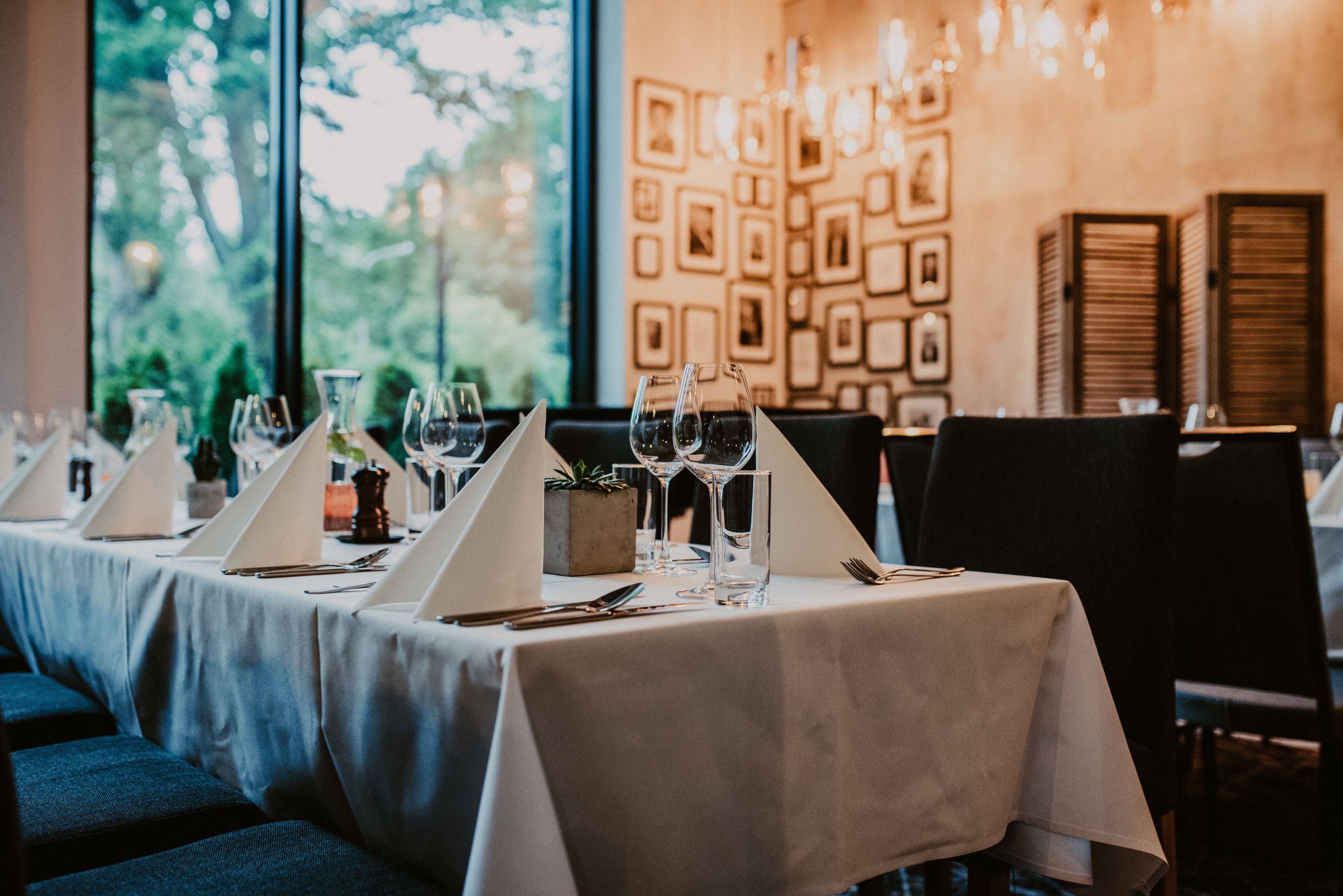 Un restaurante con mesas dispuestas para comer, cuadros en la pared y vistas a zonas verdes al exterior.