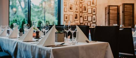 Un restaurante con mesas dispuestas para comer, cuadros en la pared y vistas a zonas verdes al exterior.