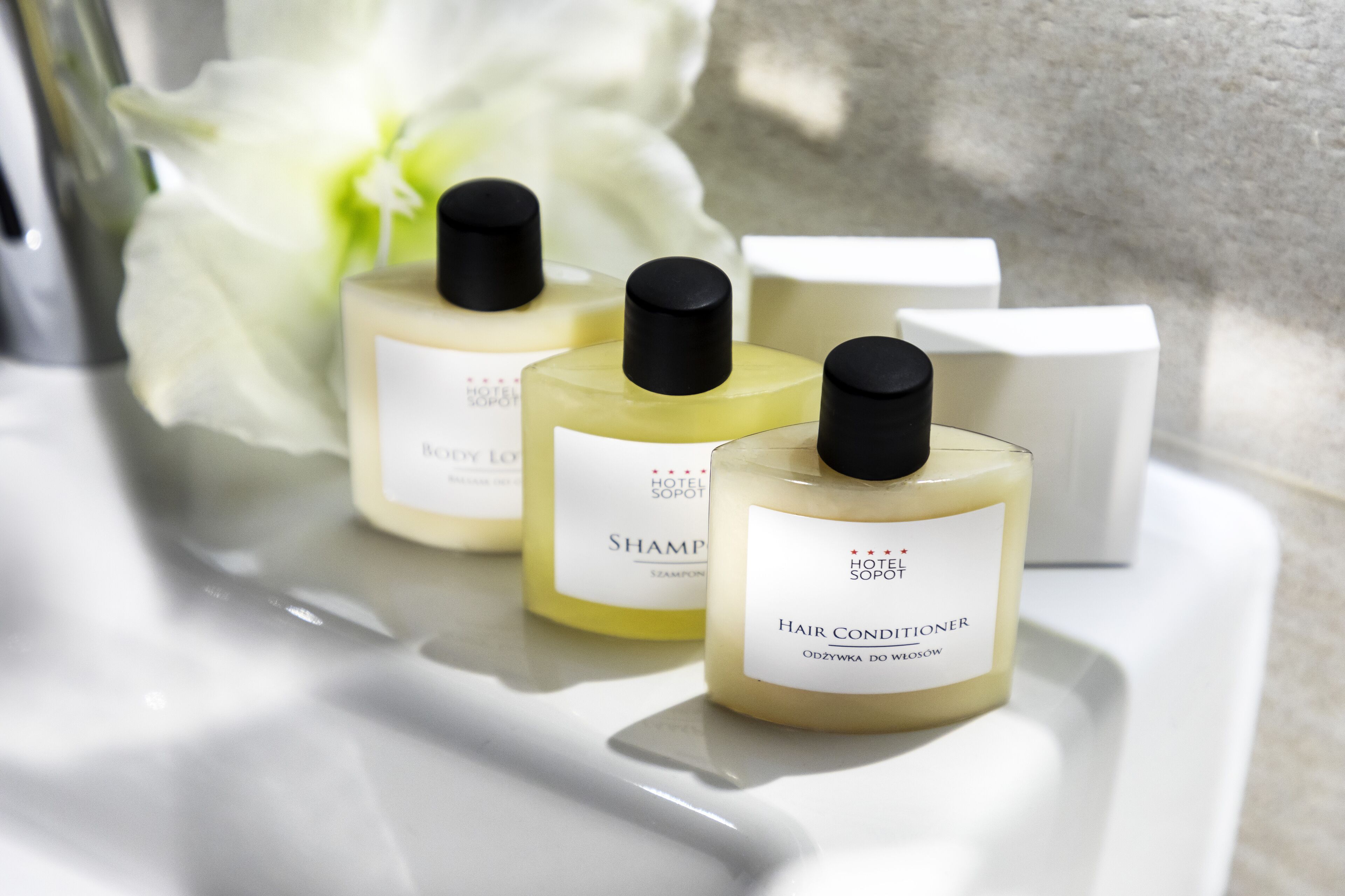 Three bottles of hair conditioner on a white countertop with a white flower in the background.