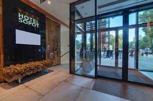 A hotel entrance with a reception desk, a large glass door, and a view of the outdoor area.