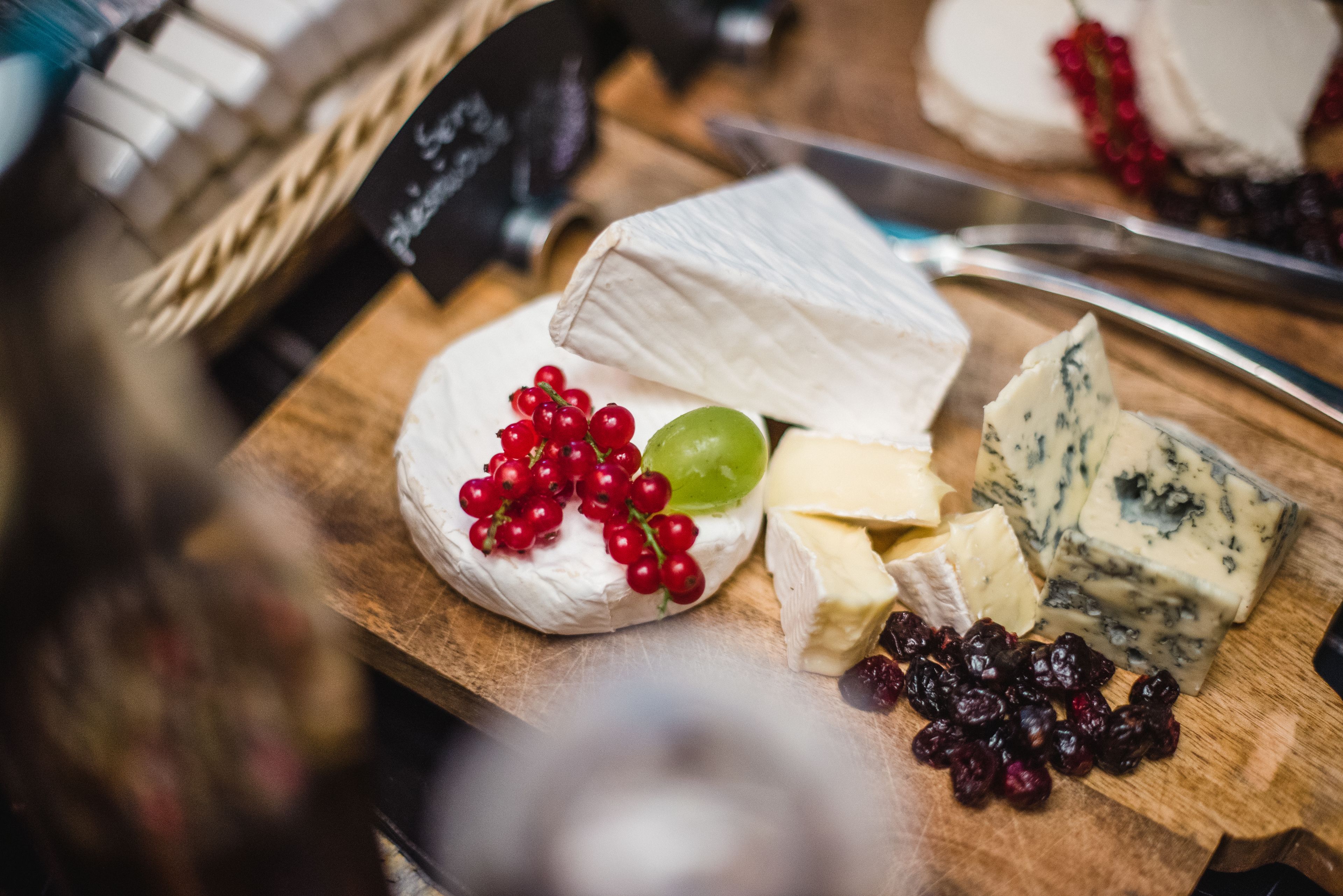 A wooden board with various cheeses, grapes, and cranberries.