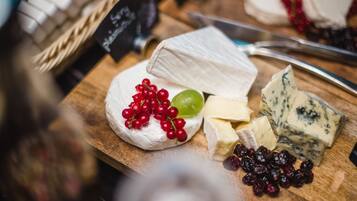 A wooden board with various cheeses, grapes, and cranberries.