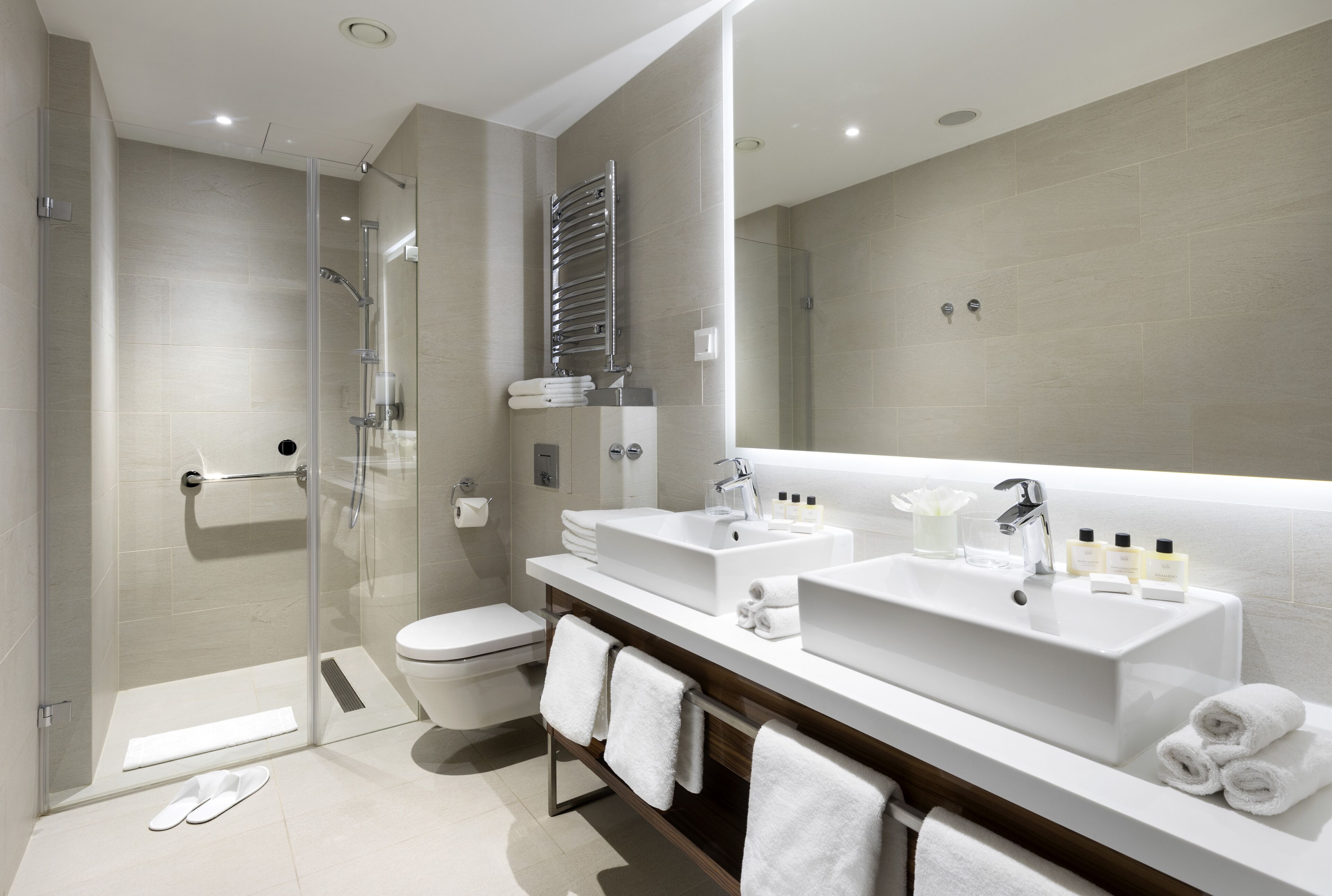 A modern bathroom with a glass shower enclosure, a toilet, and a vanity with two sinks and a large mirror.