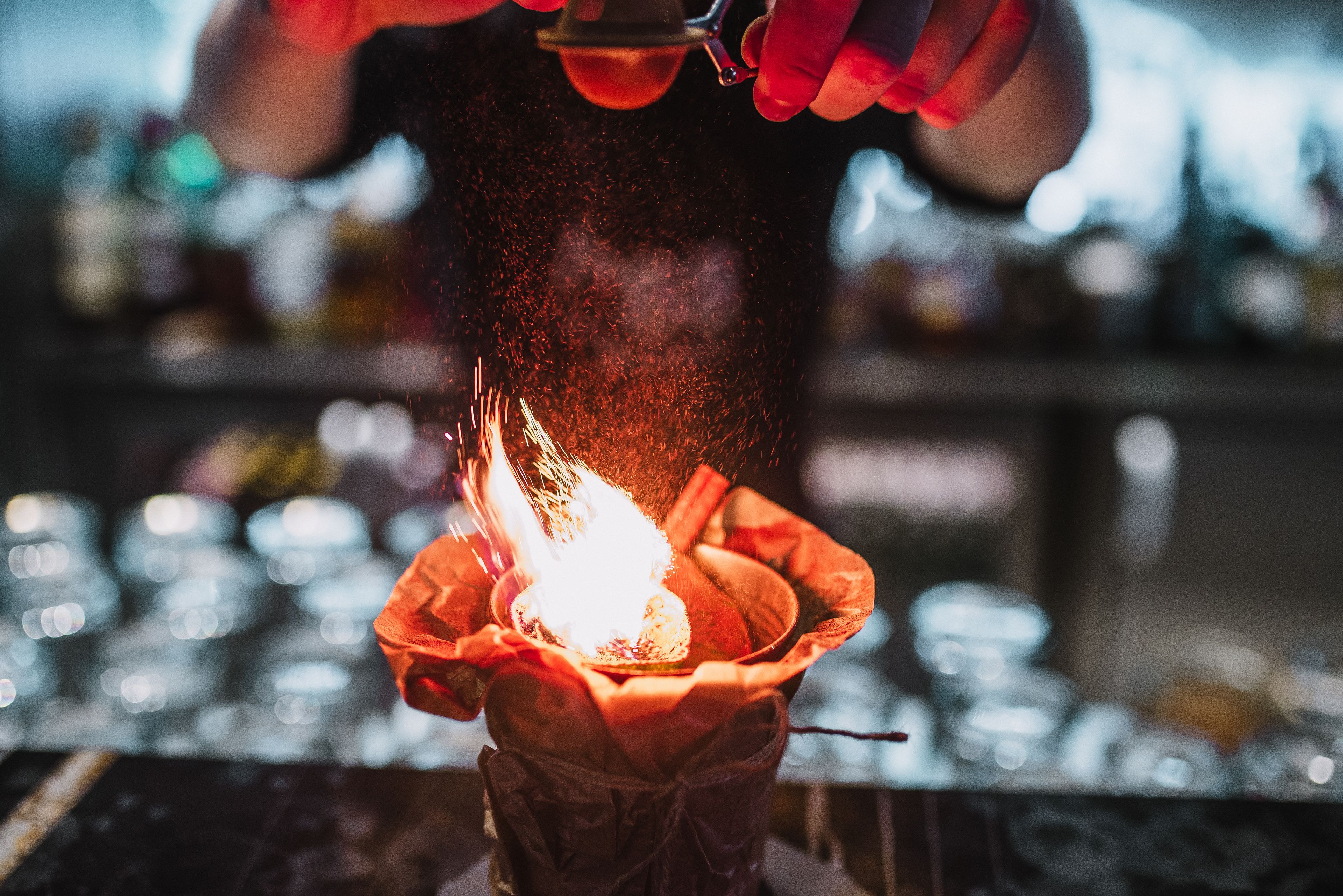 A person holding a lit candle in a glass holder.