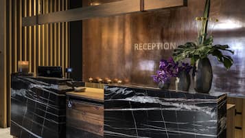 A reception desk with a marble top, a wooden panel wall, and a plant with purple flowers.