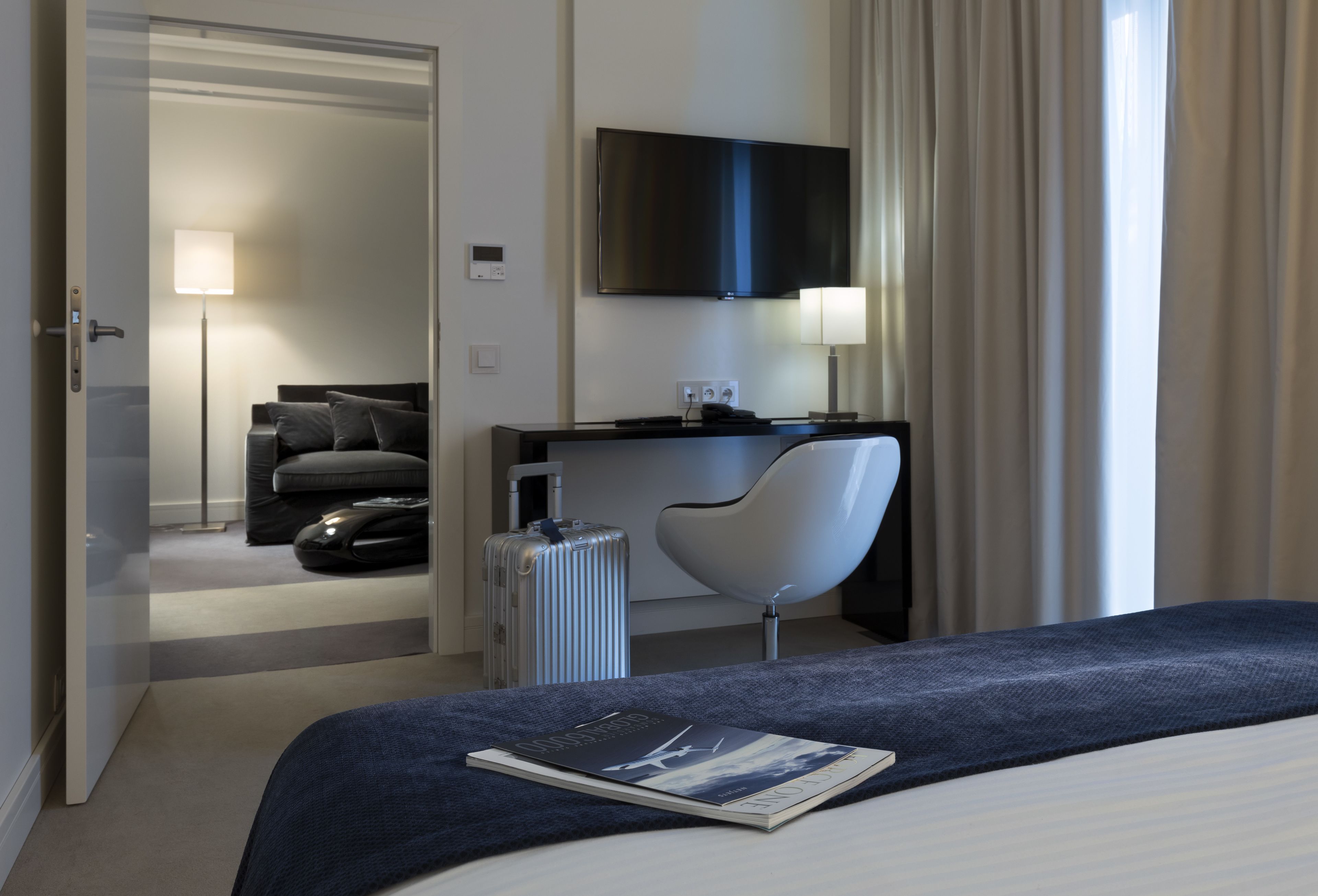 Une chambre d’hôtel moderne équipée d’un lit, d’un bureau, d’une chaise, d’une télévision et d’une valise.