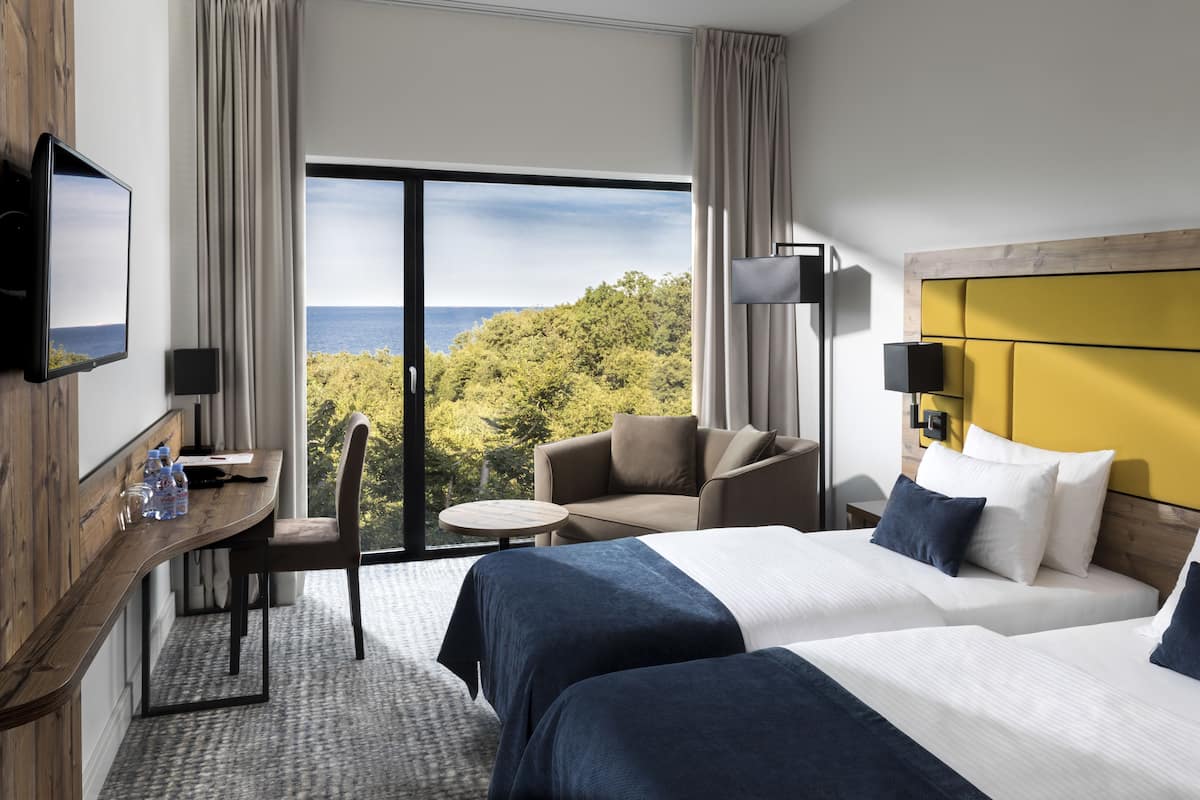 Ein Hotelzimmer mit zwei Betten, einem Schreibtisch mit Stuhl, einem Fernseher und Blick ins Freie.