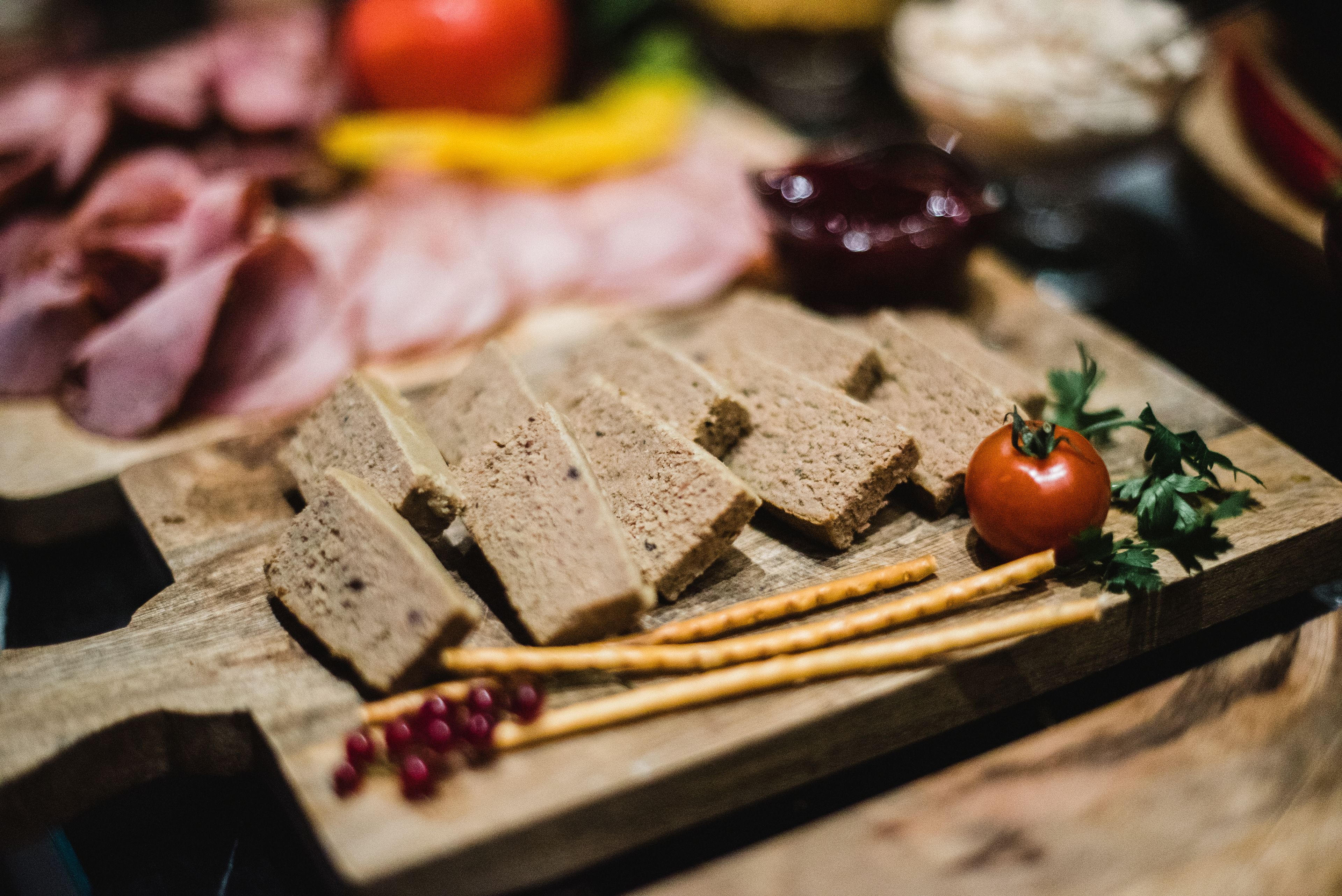 A wooden board with sliced bread, a tomato, and some red berries.