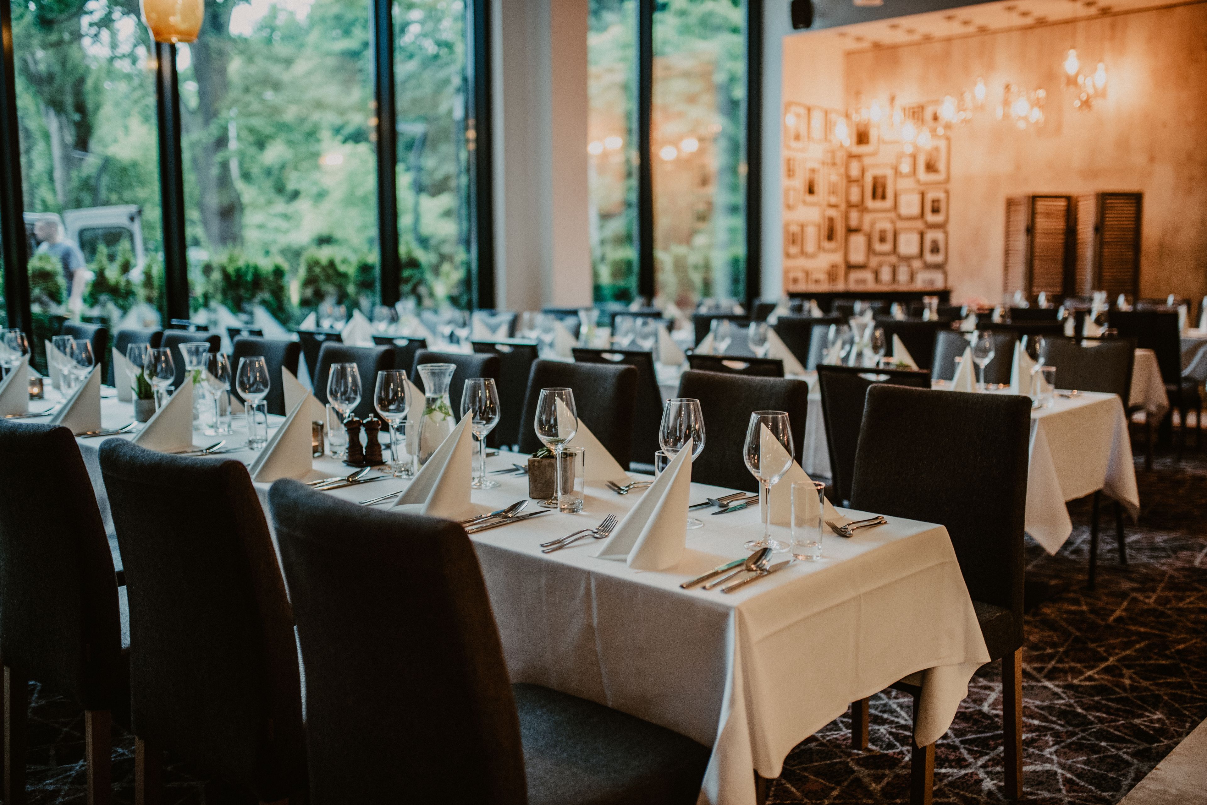 Un restaurante con mesas dispuestas para comer, ventanas amplias y vistas al verdor exterior.