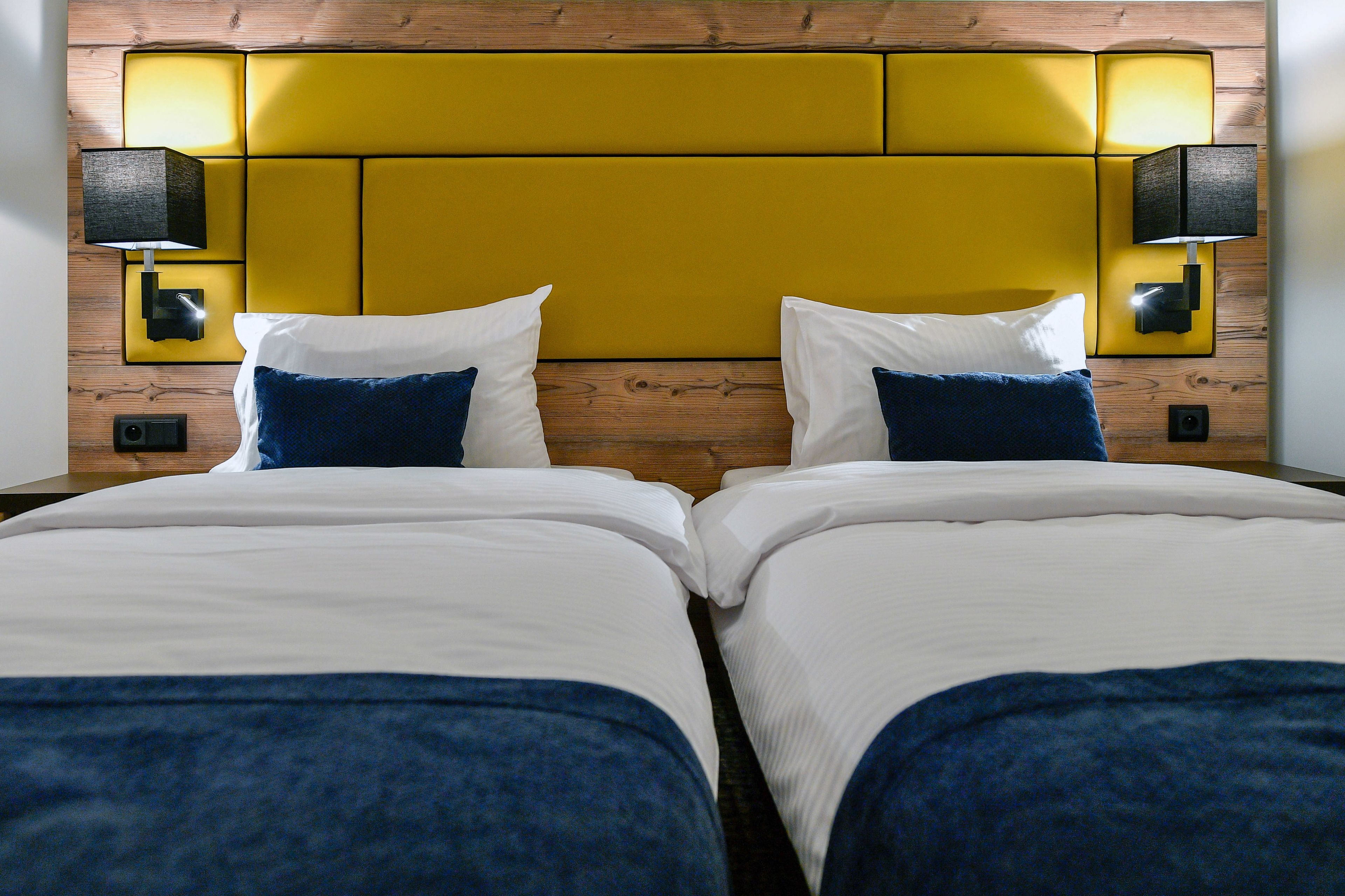 A double bed with white and blue bedding, a wooden headboard, and two wall-mounted lamps.