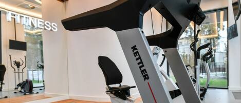 Un gimnasio con caminadora, bicicletas estáticas y un cartel en la pared que dice 'FITNESS'.