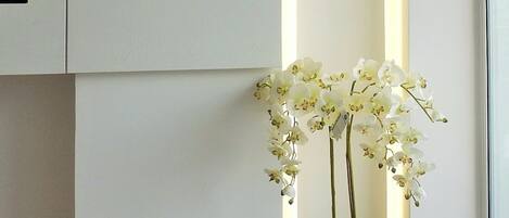 A modern interior with a vertical light panel, a white orchid plant, and a white cabinet.