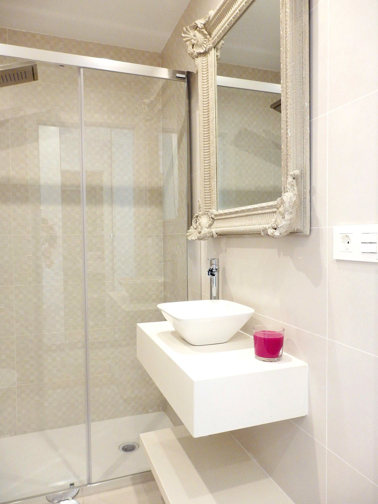 Ein modernes Badezimmer mit Duschkabine aus Glas, einem weißen Waschbecken mit Schale und einem Spiegel mit aufwendigem Rahmen.