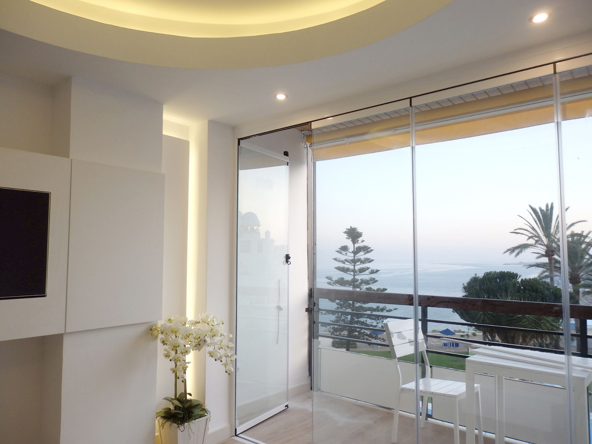 Een modern balkon met een glazen deur, een witte stoel en een potorkidee.