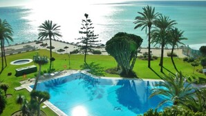A swimming pool surrounded by palm trees and a view of the ocean. - Waterfront Santa Clara Apartments (Torremolinos)