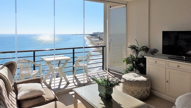 A balcony with a view of the sea, a sofa, a TV, and a dining table. - Waterfront Santa Clara Apartments (Torremolinos)