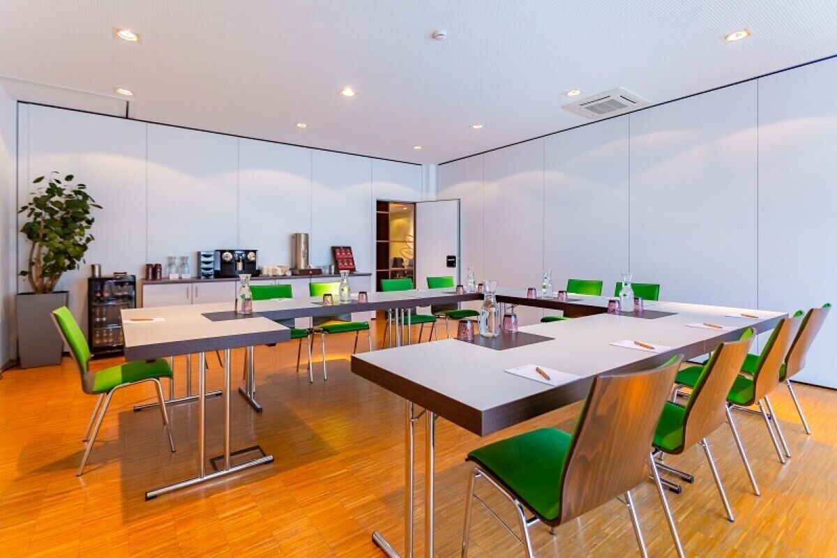 Una sala de conferencias con una larga mesa, sillas verdes y una planta.