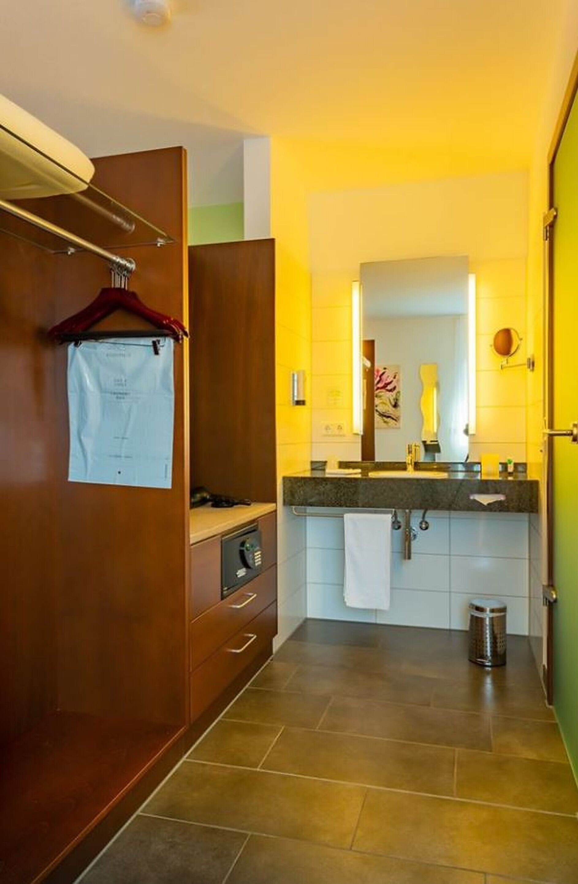 A hotel bathroom with a wooden wardrobe, a mirror, a sink, and a towel hanging on the wall.