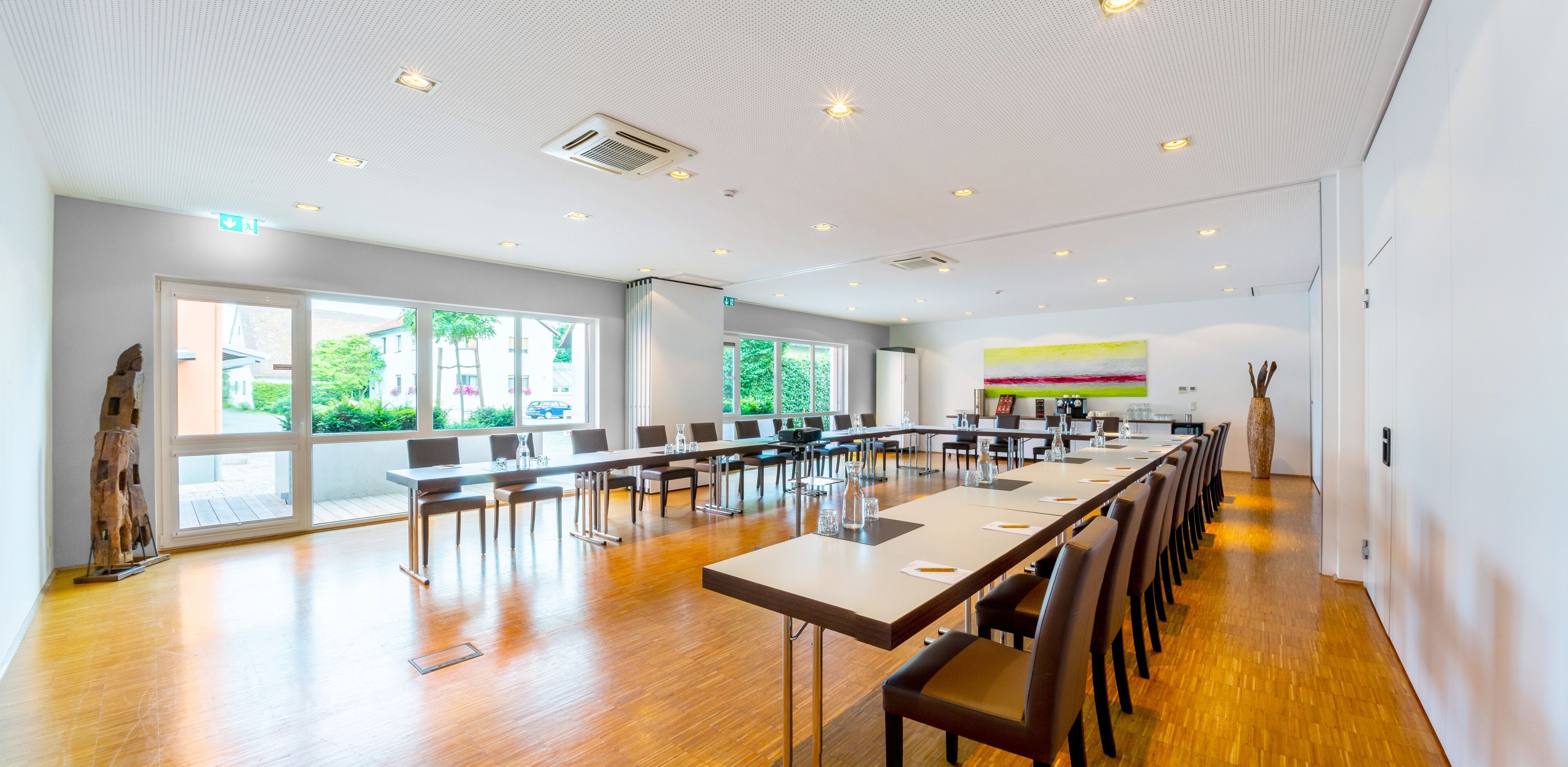 A spacious conference room with long tables and chairs, large windows, and a modern ceiling design.