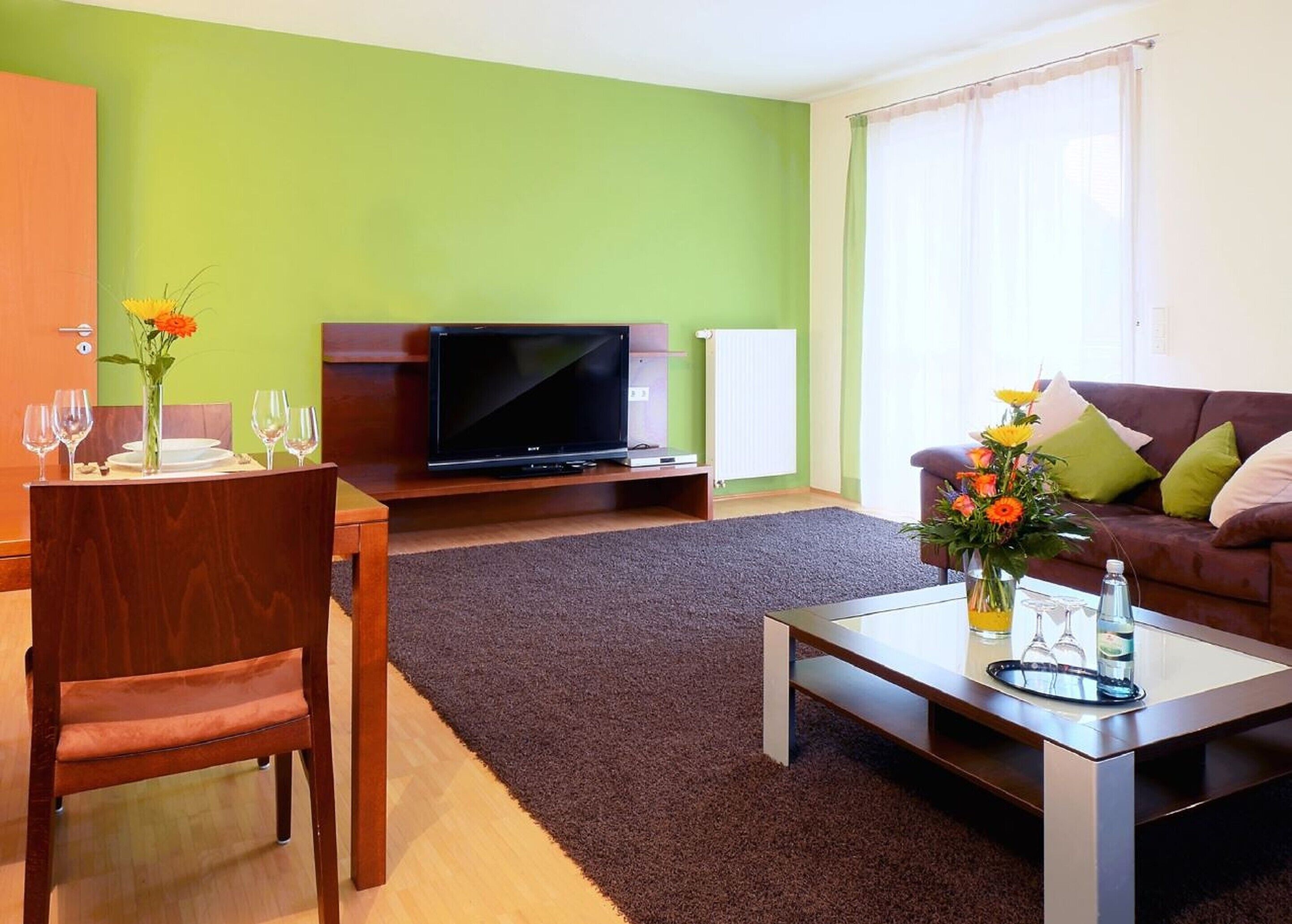 A living room with a television, a dining table with chairs, a sofa, and a coffee table.