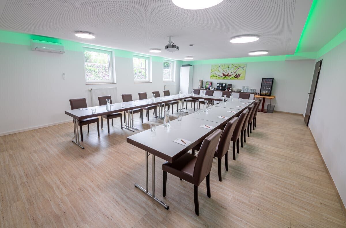 Een vergaderzaal met een lange tafel, stoelen, een projectiescherm en een schilderij aan de muur.