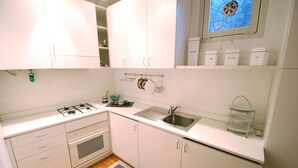 A compact kitchen with white cabinets, a gas stove, a sink, and a window with a decorative view. - San Rocco (Venice)