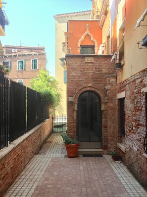 Un carrer estret amb una entrada de maó, una planta en test i una tanca de metall negre.