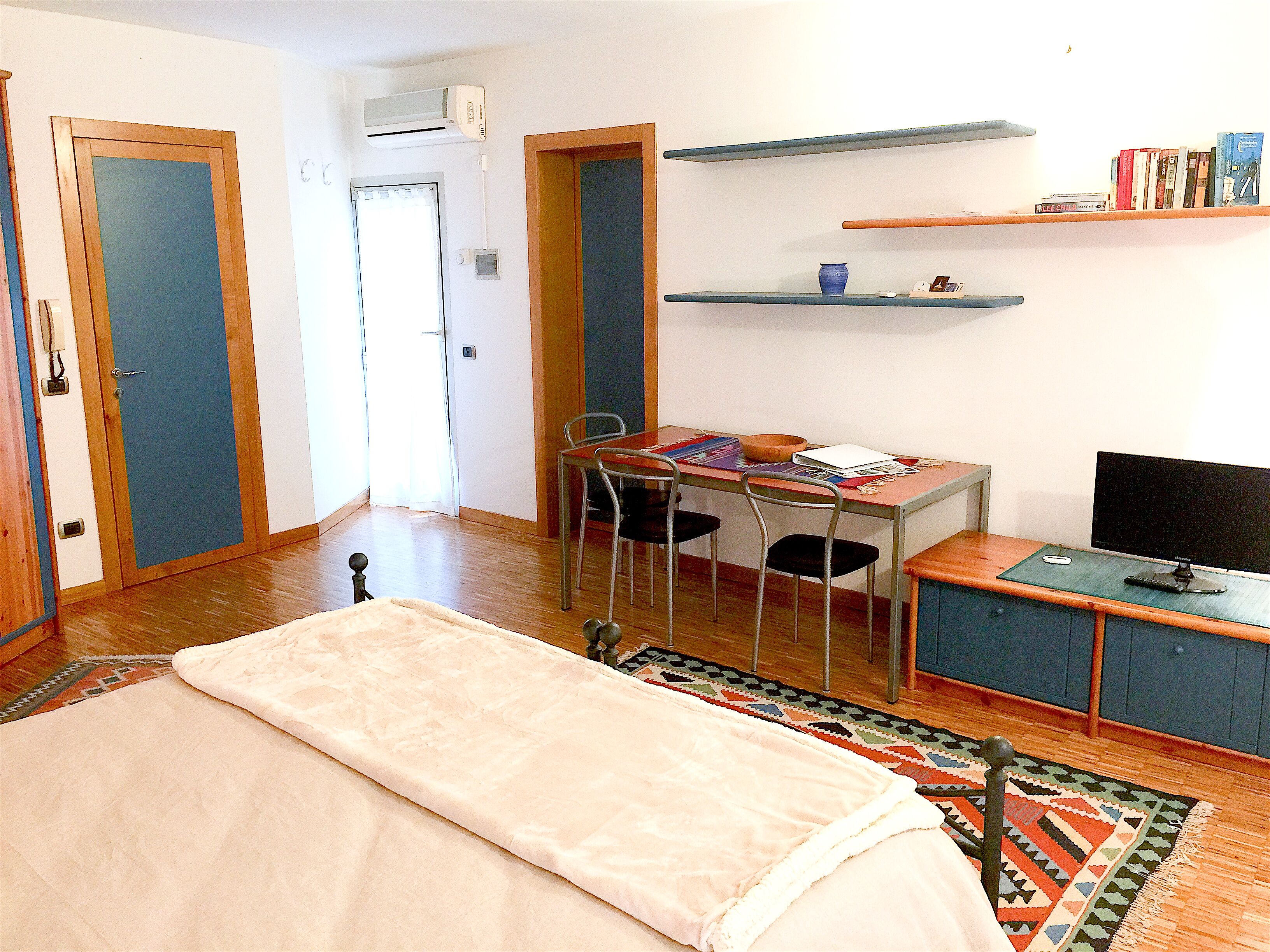 Une pièce comprenant un lit, un bureau avec un ordinateur, une chaise, une bibliothèque et une porte.