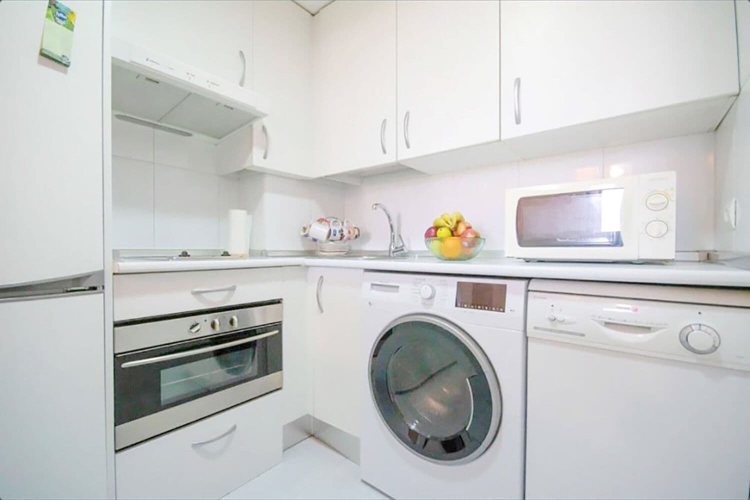 A compact kitchen with a built-in oven, a washing machine, and a microwave.