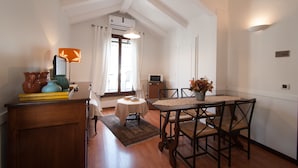 Un coin repas avec une table et des chaises, une petite table ronde recouverte d’une nappe et un vase rempli de fleurs.