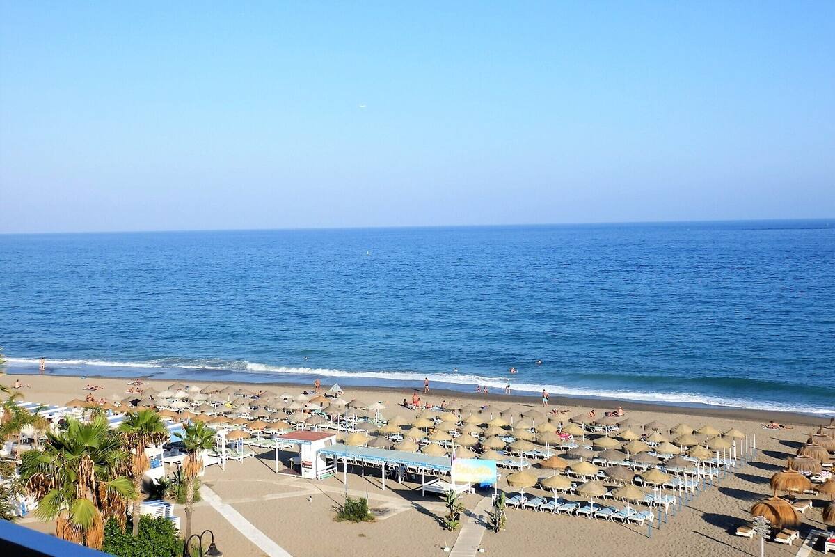 Una platja amb ombrelles i gandules, cel blau i l'oceà.