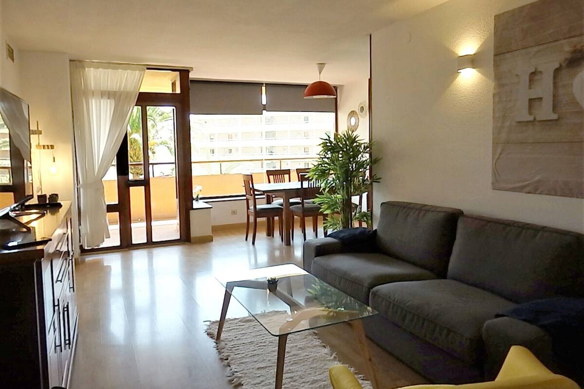 Un saló modern amb una taula de centre de vidre, un sofà gris i una zona de menjador amb una taula i cadires.
