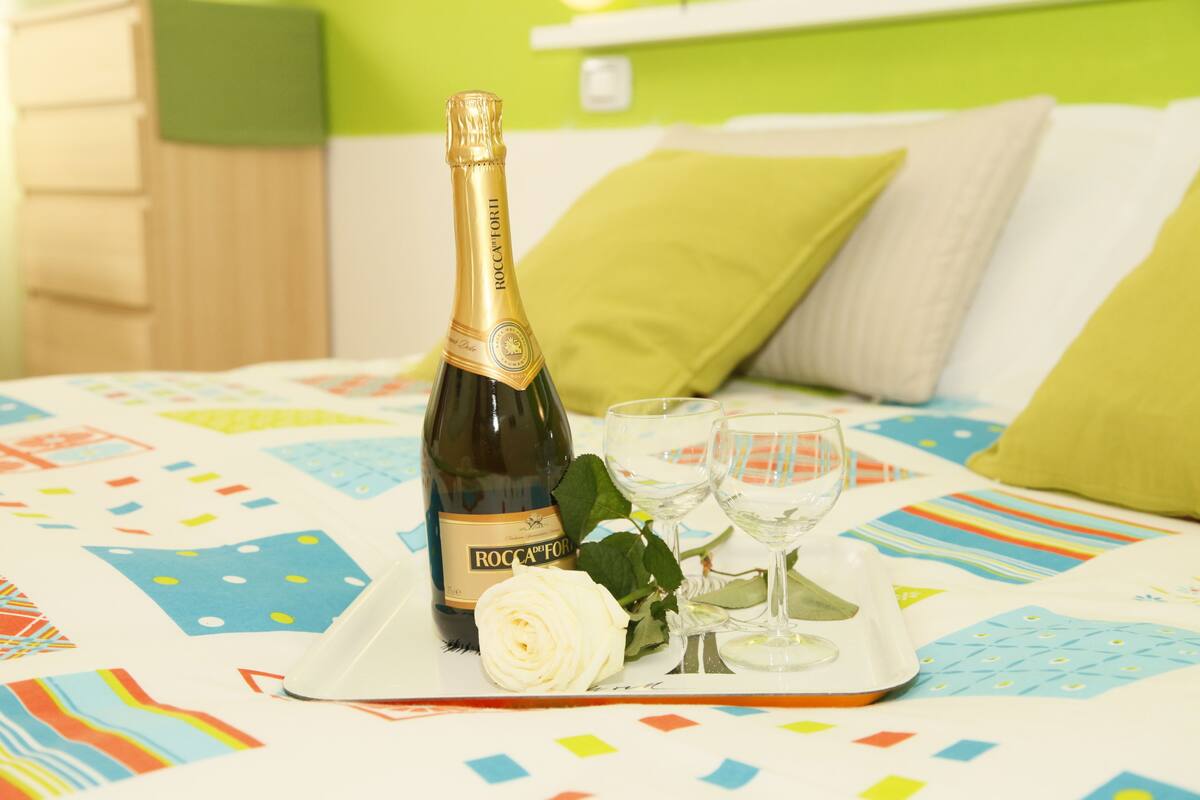 A bottle of Roccaforte wine, two wine glasses, and a white rose on a tray on a bed with a colorful geometric-patterned bedspread.