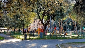 Ein Park mit einem gepflasterten Weg, Spielgeräten und einem Gebäude im Hintergrund.