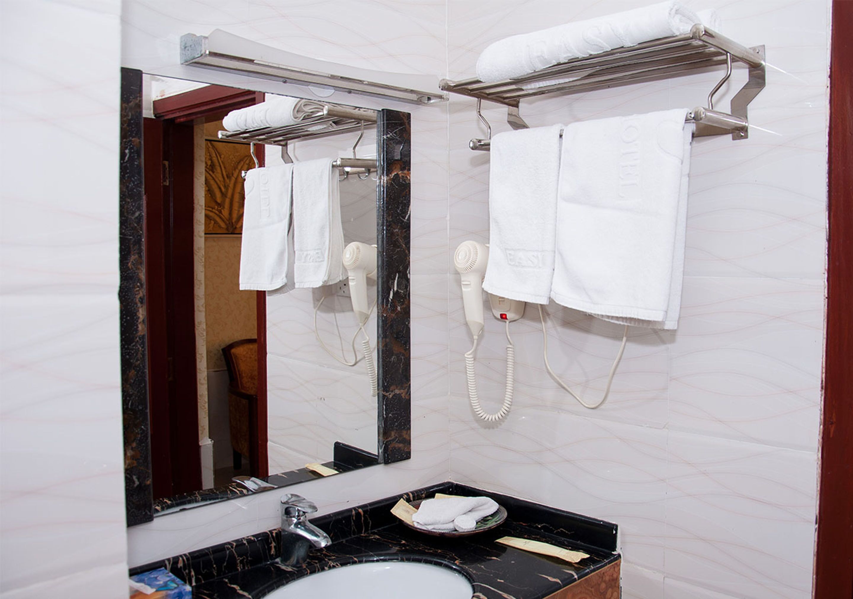 A bathroom with a large mirror, a sink, a hairdryer, and a towel rack.