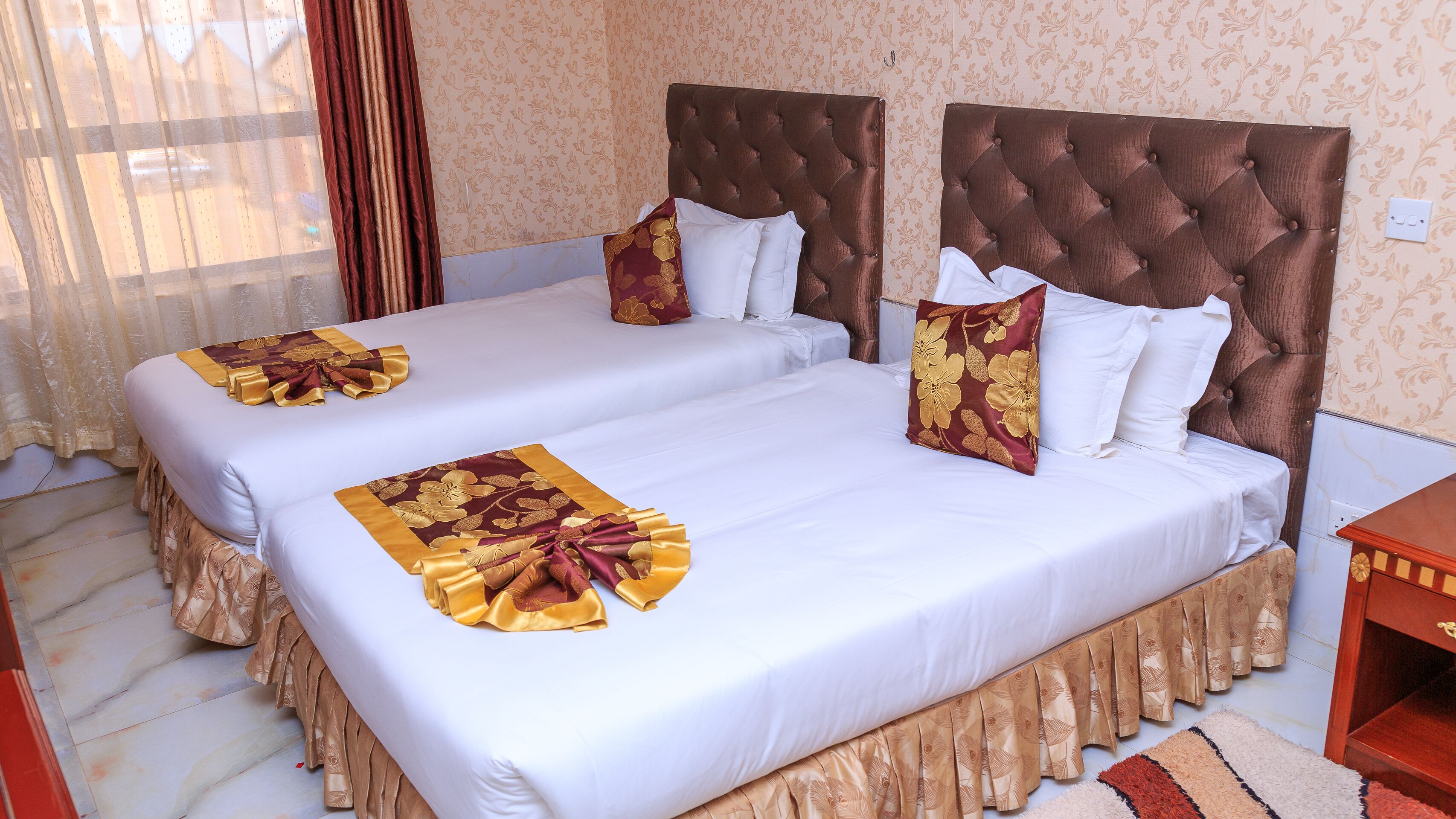 A hotel room with two beds, each with a tufted headboard, white bedding, and decorative pillows.