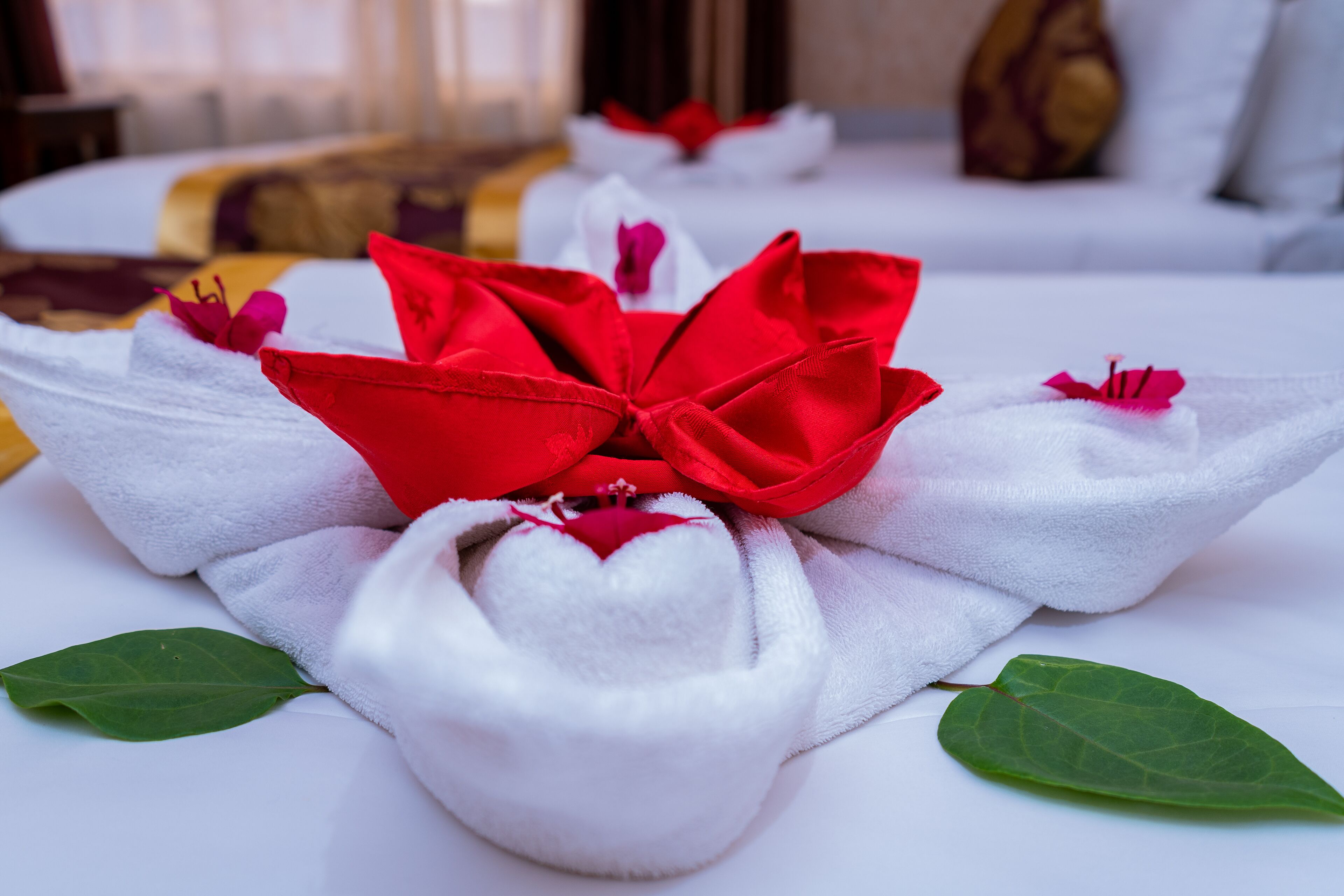 A neatly arranged towel with a red bow and a heart-shaped pillow on a bed.