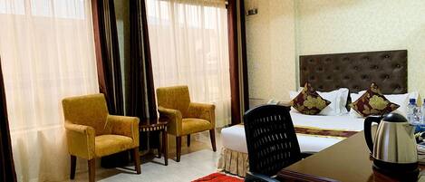 A hotel room with a bed, two armchairs, a desk, and a coffee maker.