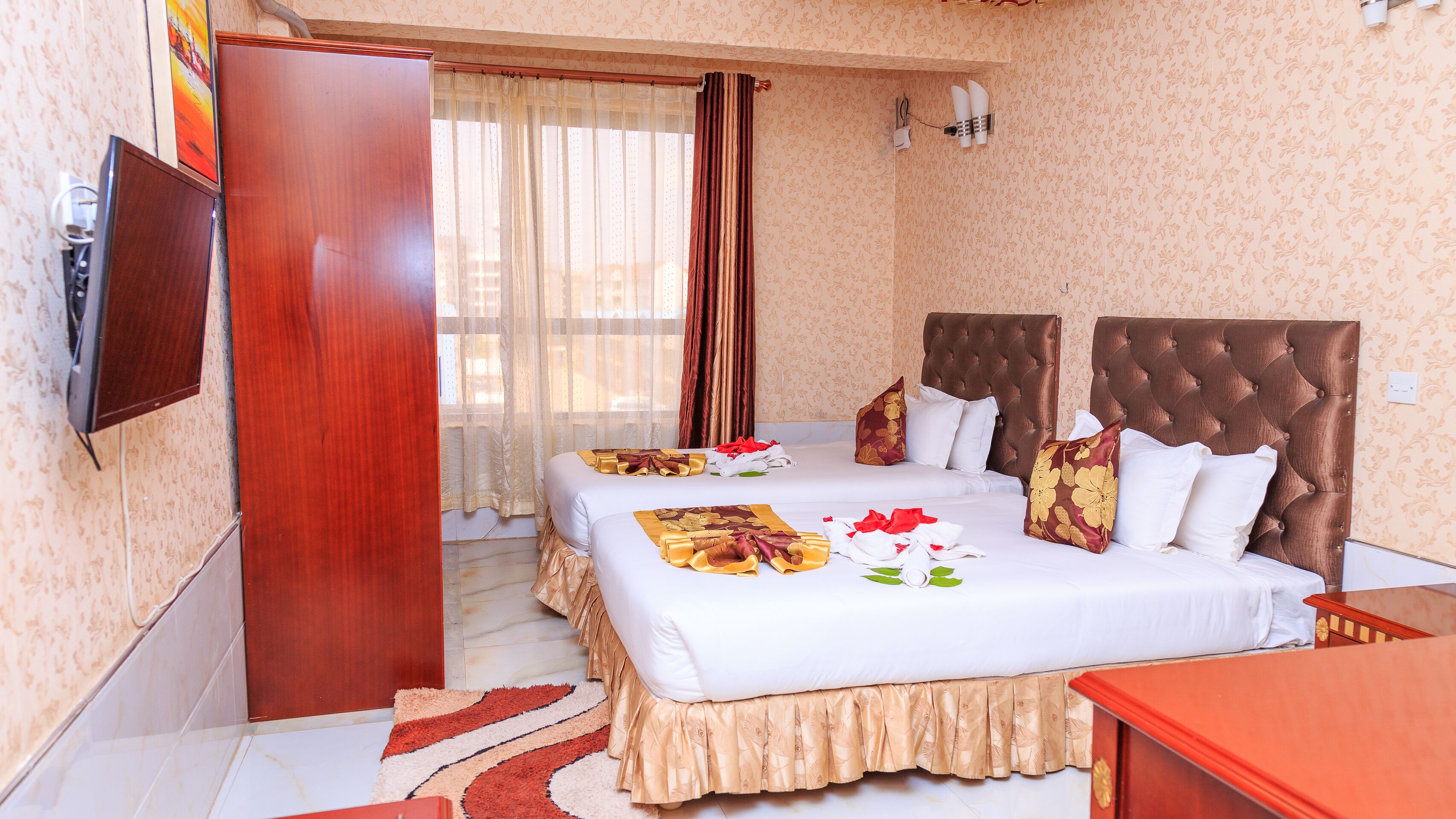 A hotel room with two beds, a TV, and a wooden wardrobe.