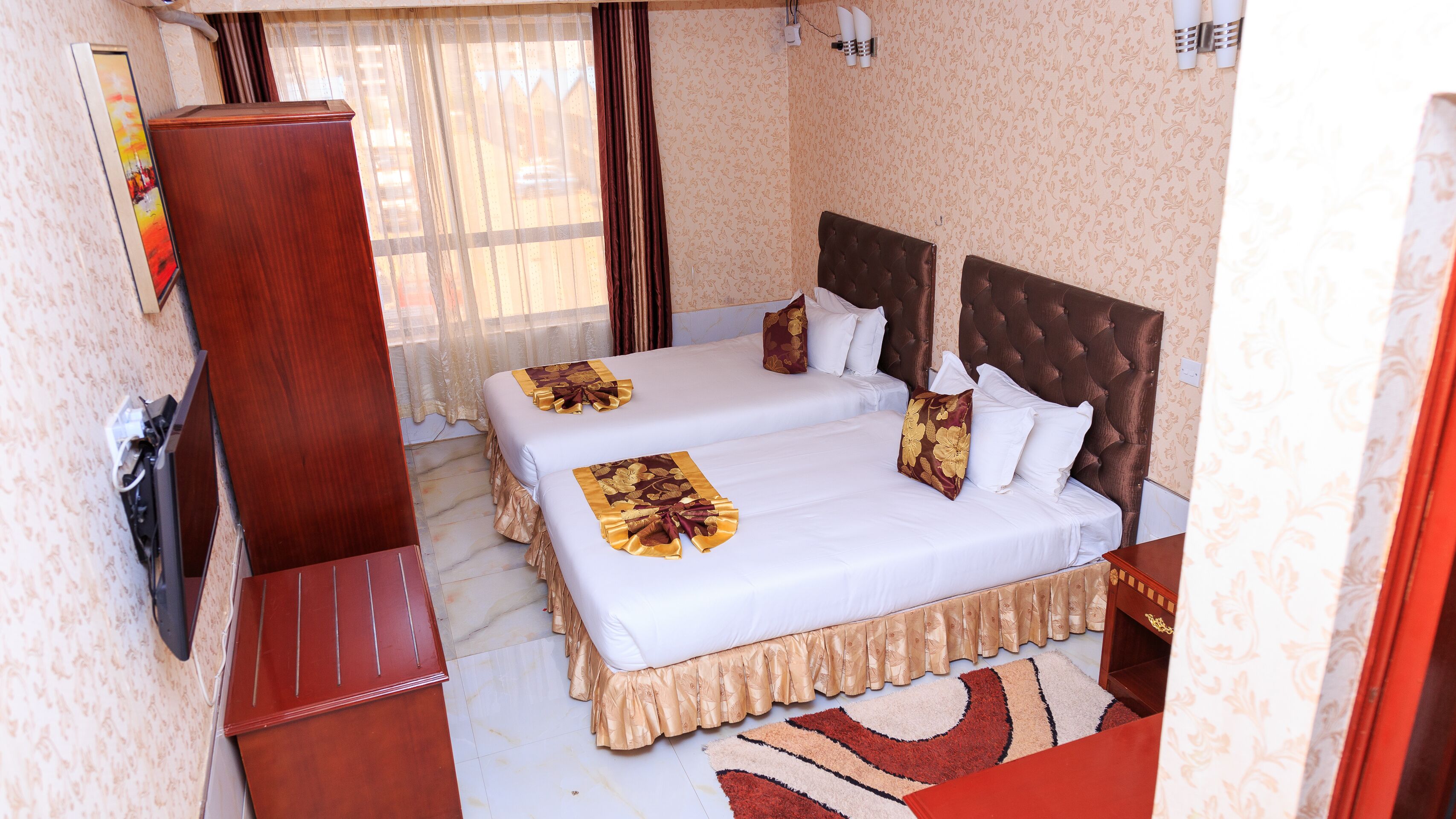 A hotel room with two beds, a wooden desk, a TV, and a patterned carpet.