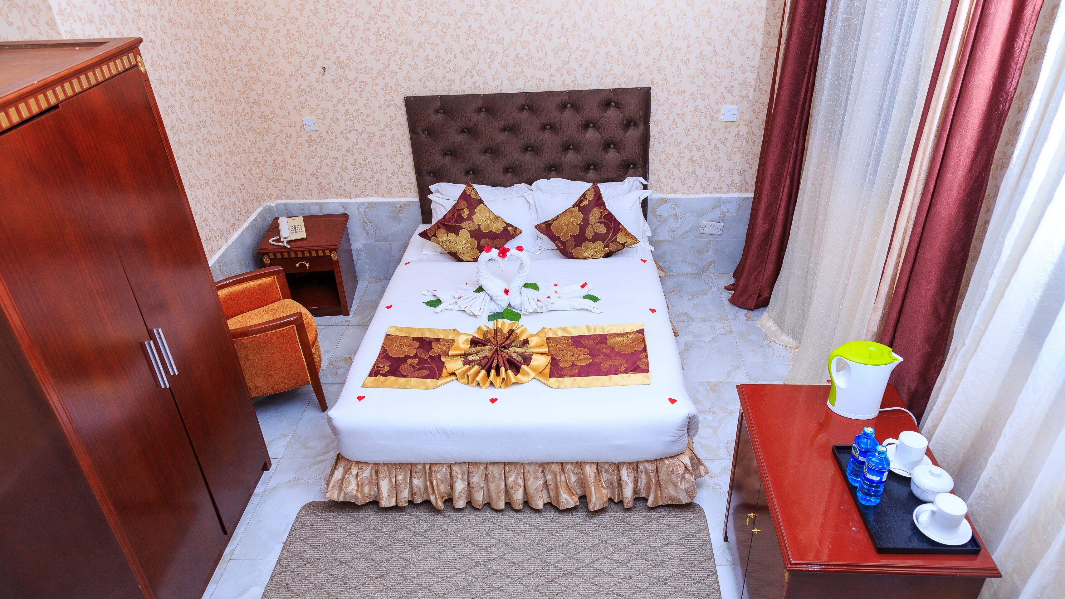 Una camera d'albergo ordinata con un letto, un armadio, un tavolino con il telefono e un vassoio con bottigliette d'acqua e bicchieri.