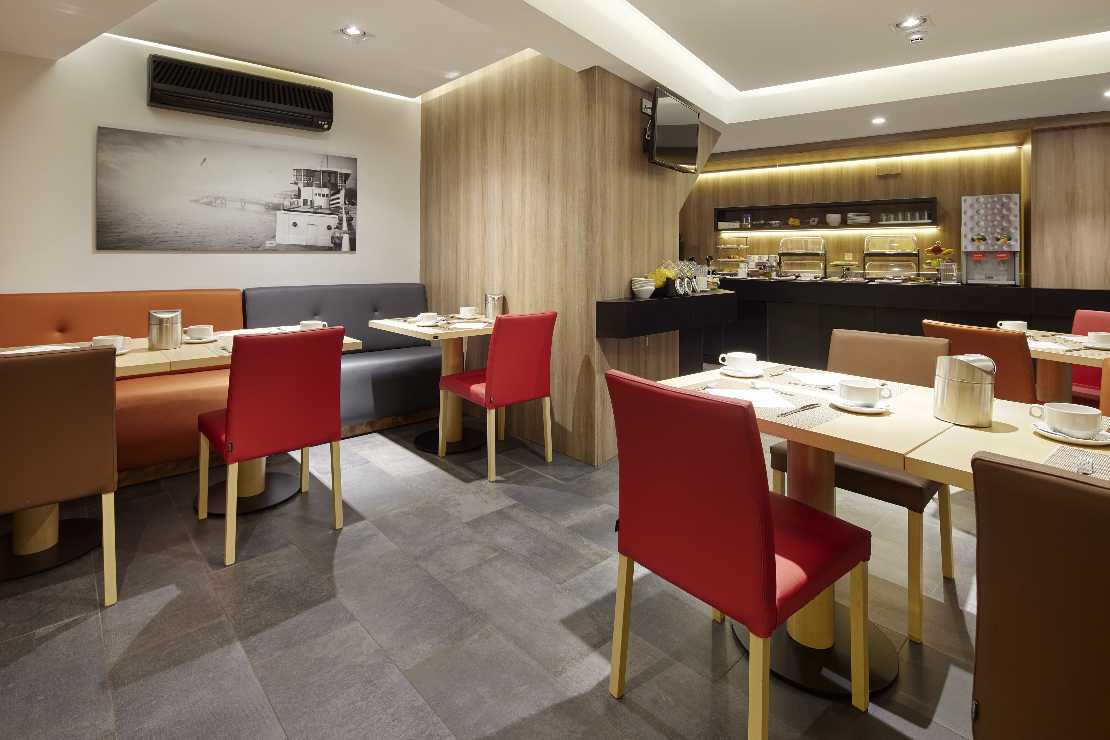 A modern dining area with booths and tables, a kitchen counter with appliances, and a large window with a view.