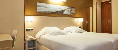 Habitación de hotel con una cama grande, lámparas de noche, una mesita de noche con teléfono y un cuadro colgado en la pared.