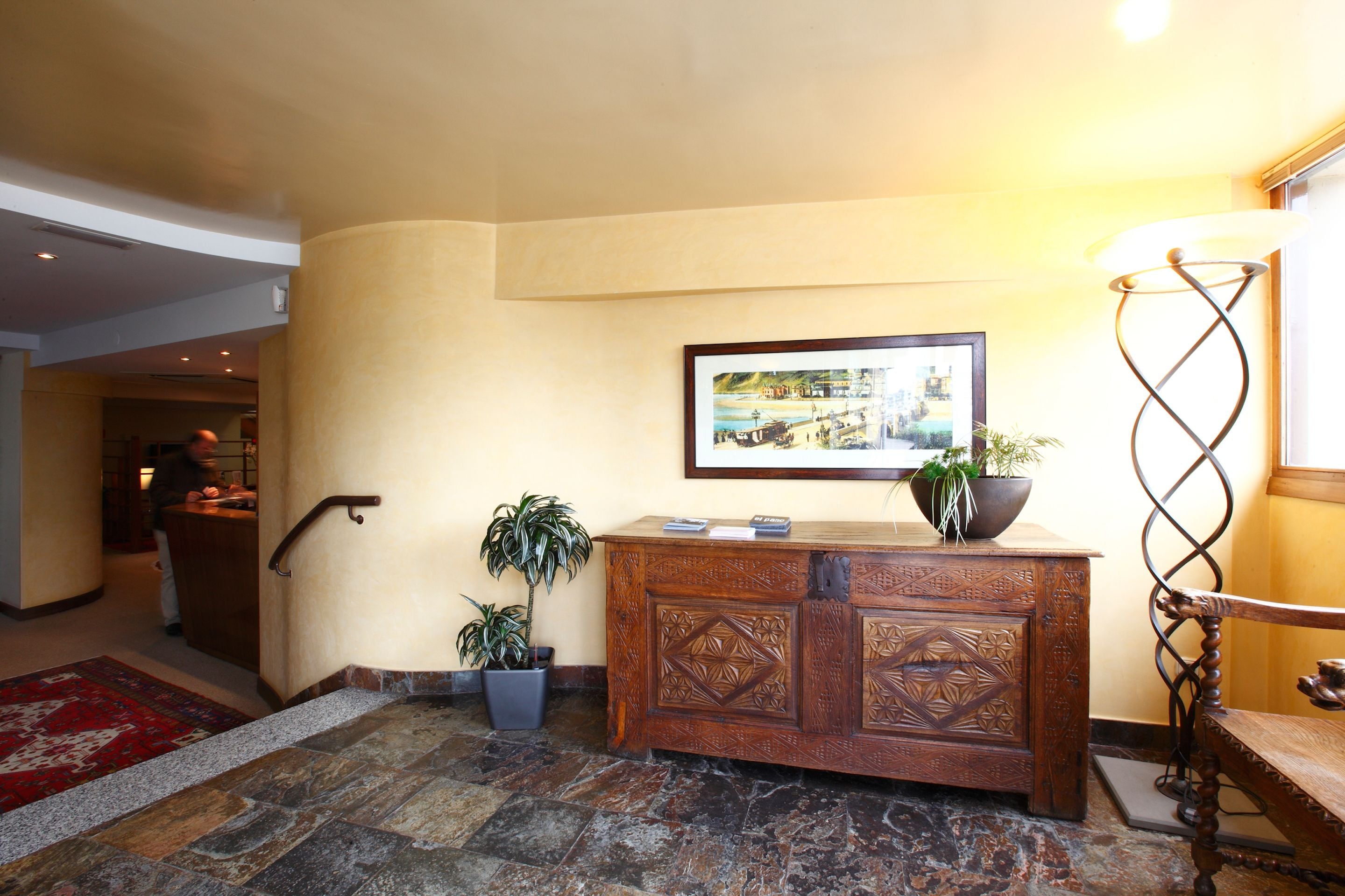 A reception area with a wooden desk, a framed picture on the wall, and a potted plant.