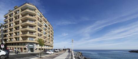A multi-story hotel with balconies, a paved walkway, and a view of the sea.