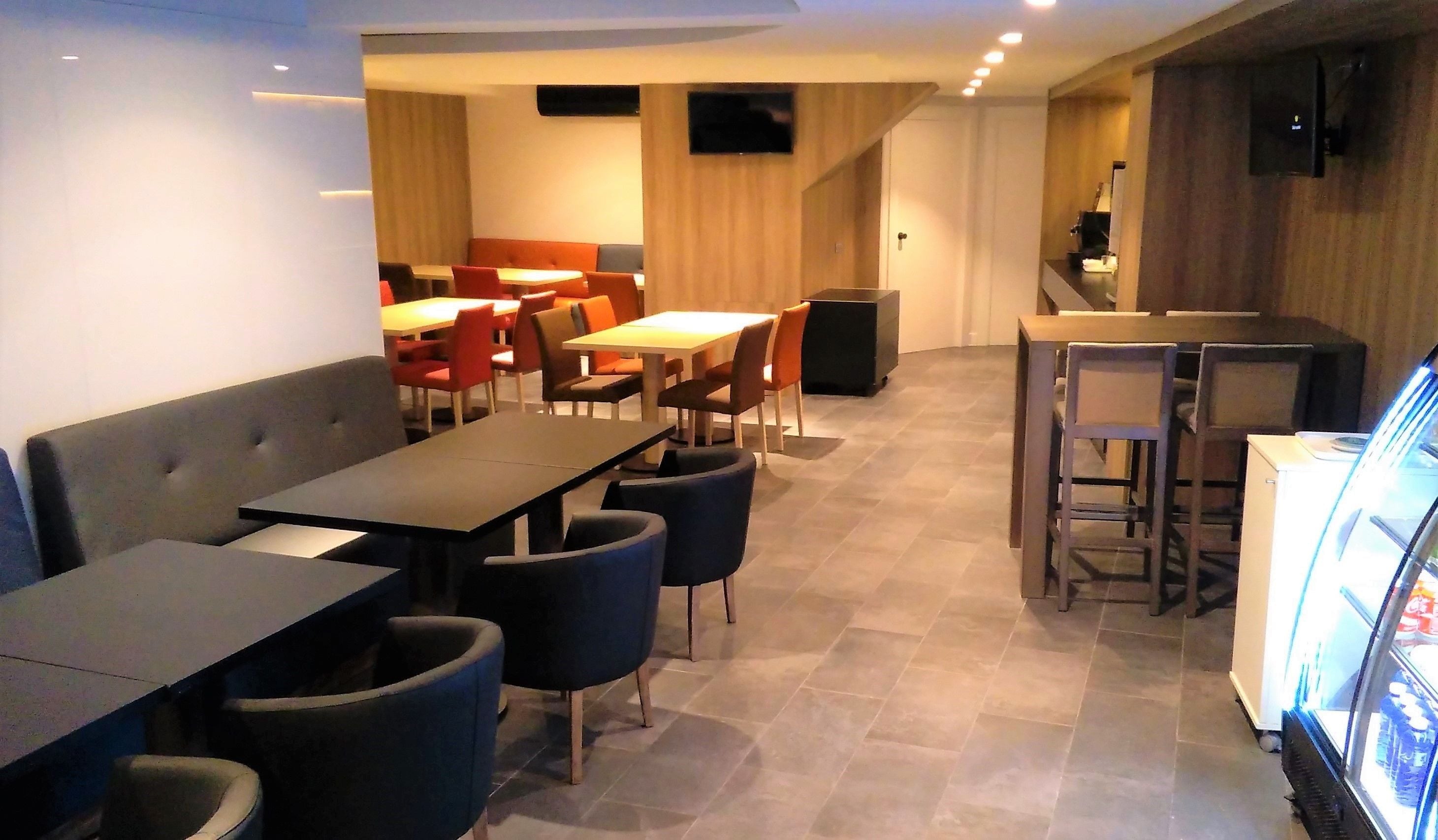 A modern dining area with multiple tables and chairs, a sofa, and a refrigerator.