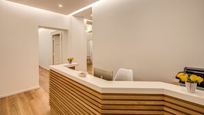 A modern reception area with a wooden reception desk, a white wall, and a mirror reflecting the interior. - Dopodomani Suite (Rome)