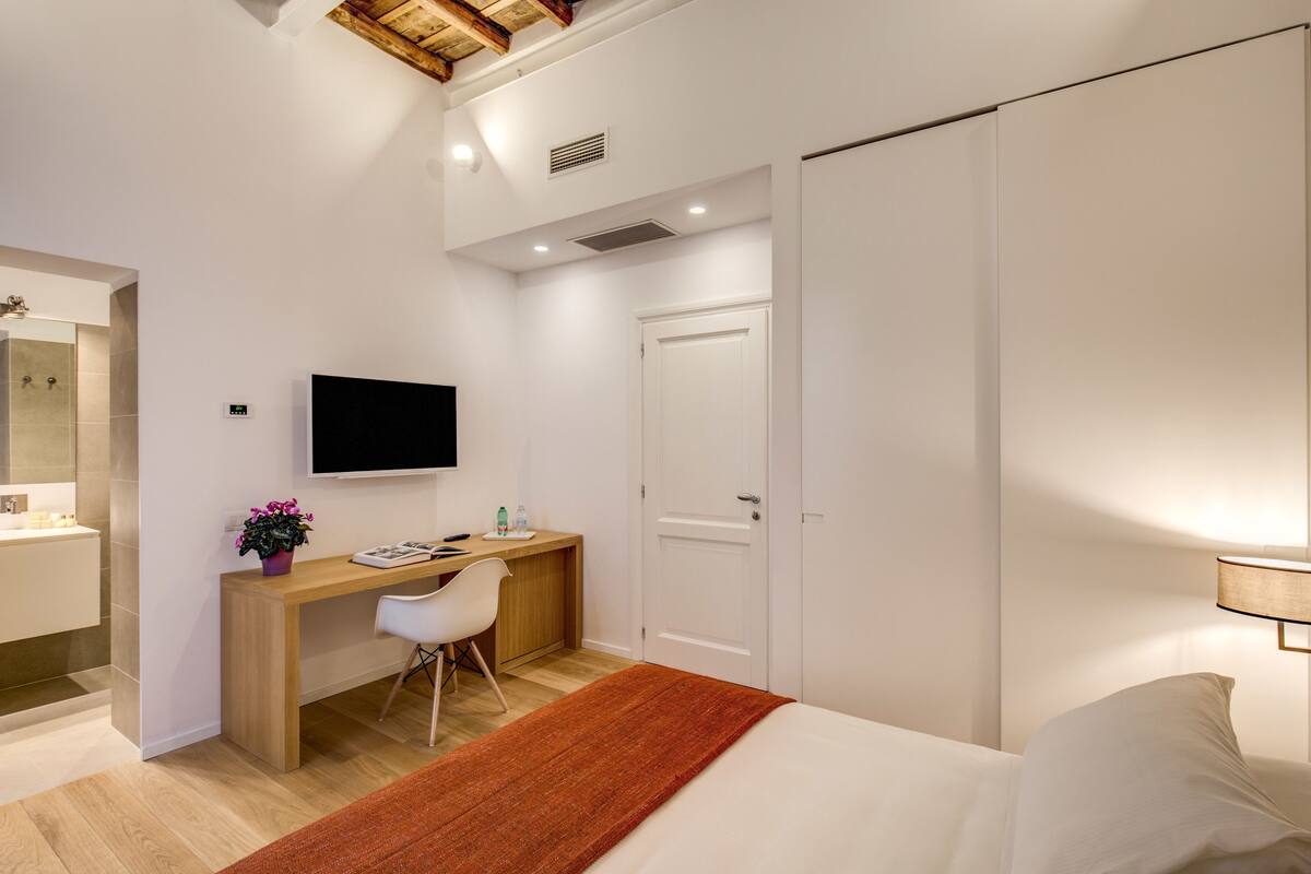 Un dormitorio moderno con cama, escritorio, silla, televisor y armario.