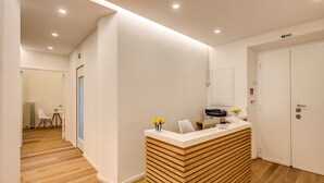 A reception area with a wooden reception desk, a white wall, and a door leading to a room. - Dopodomani Suite (Rome)